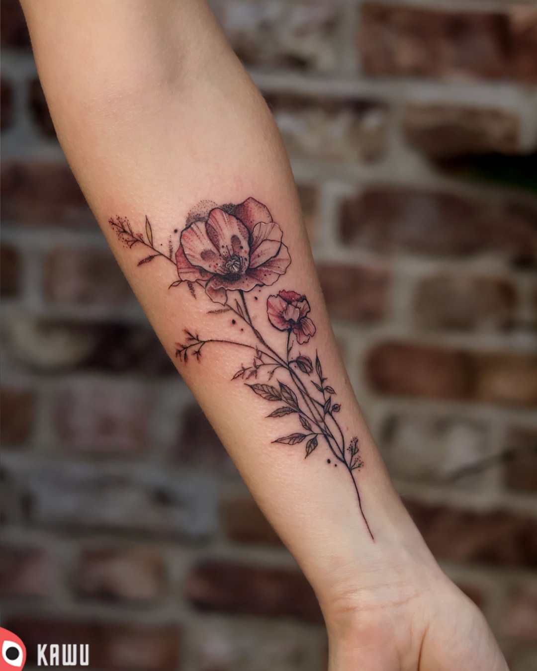 Delikatny tatuaż na przedramieniu przedstawiający kompozycję kwiatową z dominującym motywem maku w odcieniach czerwieni i czerni, wykonany techniką linearną z elementami dotwork, na tle ceglanej...