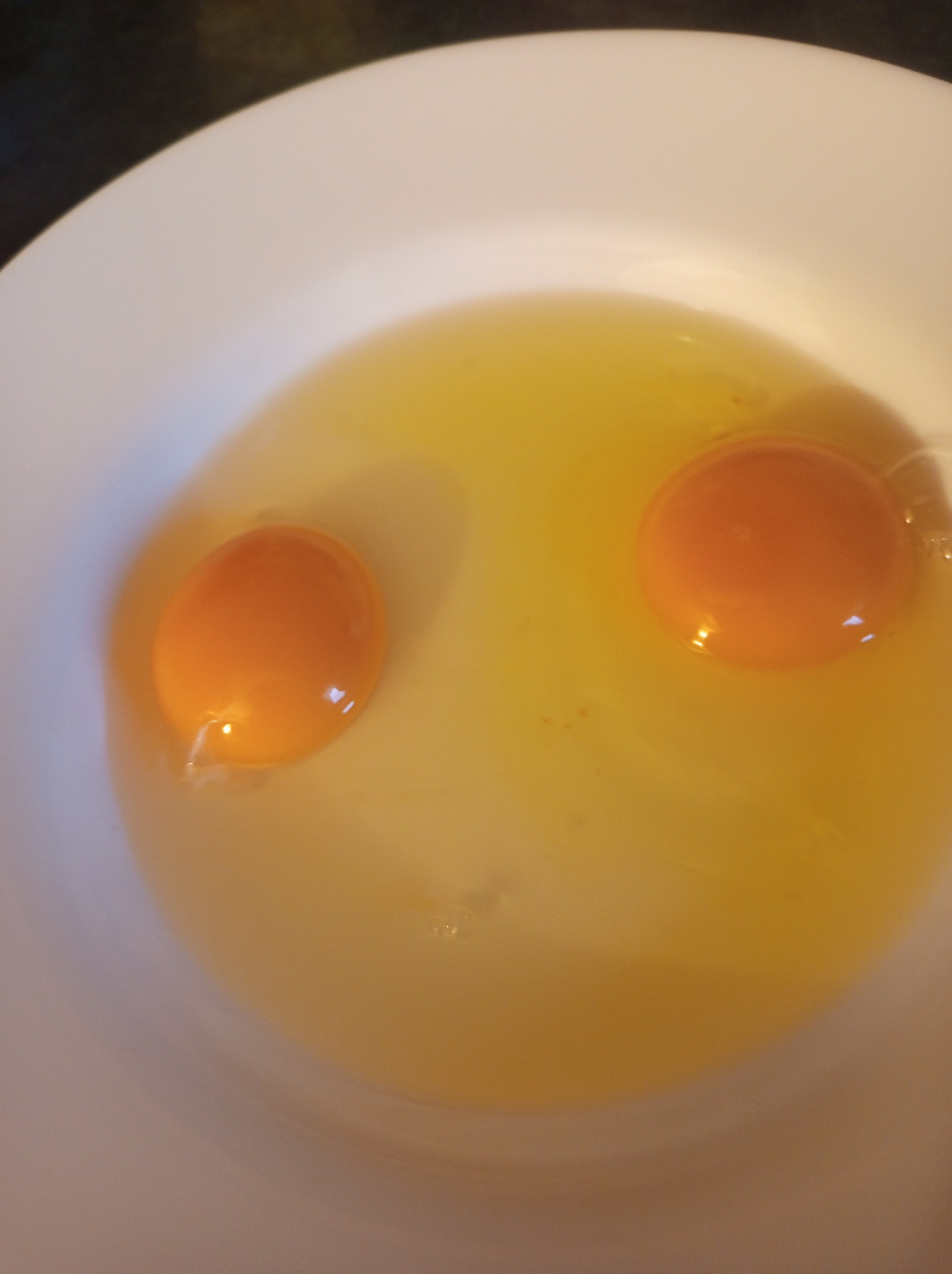 Dwa surowe żółtka jaj w białej misce, z widocznymi resztkami białka i małymi plamkami.