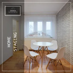 Jasne wnętrze pokoju z białym okrągłym stołem i czterema krzesłami Eames, parkiet na podłodze, ściana z cegły, aranżacja typu home staging.