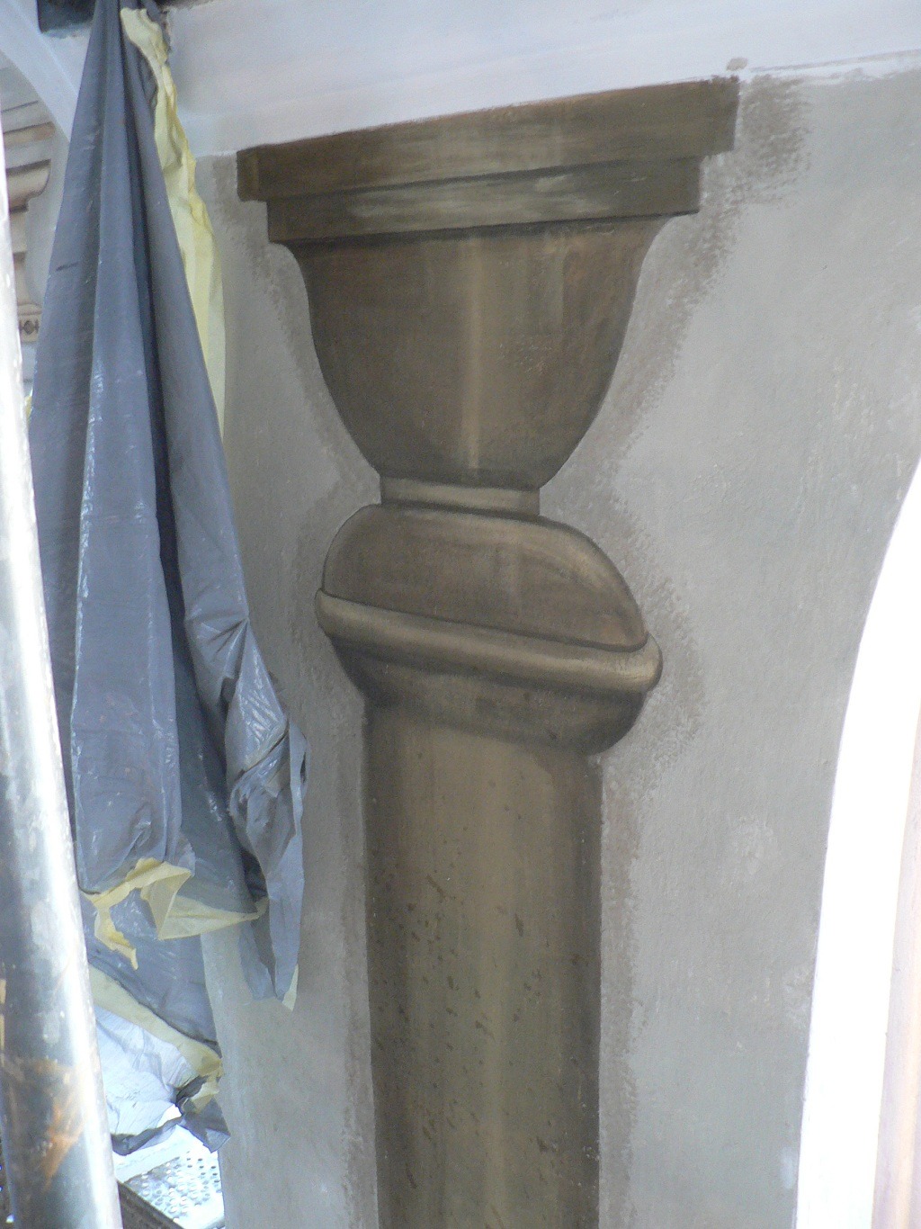 Fragment polichromii w synagodze, przedstawiający kolumnę w trakcie prac konserwatorskich, zabezpieczoną folią ochronną.