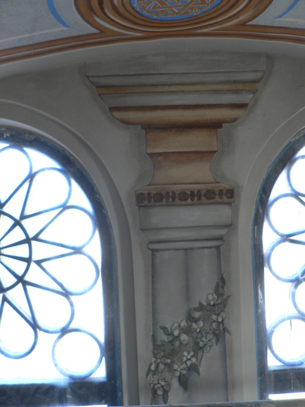 Fragment wnętrza synagogi: okna z dekoracyjnymi szprosami, malowana kolumna z motywem kwiatowym, zdobiony sufit z gwiazdą Dawida.
