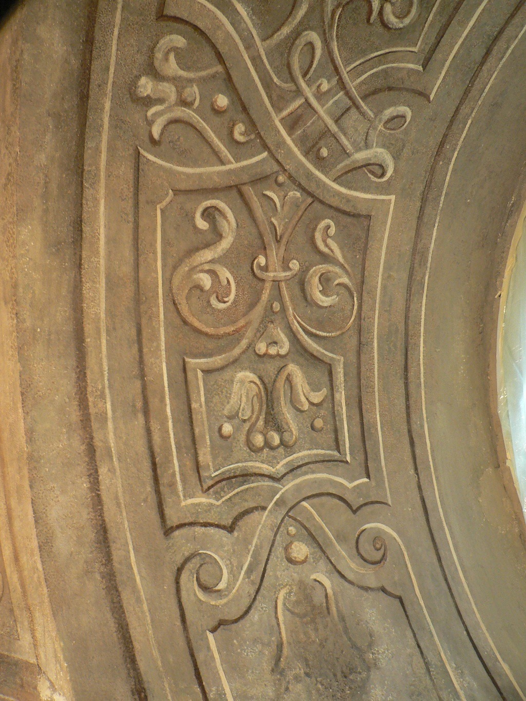 Fragment odrestaurowanej polichromii ściennej z motywami roślinnymi i geometrycznymi w odcieniach beżu i brązu, widoczny fragment łuku.