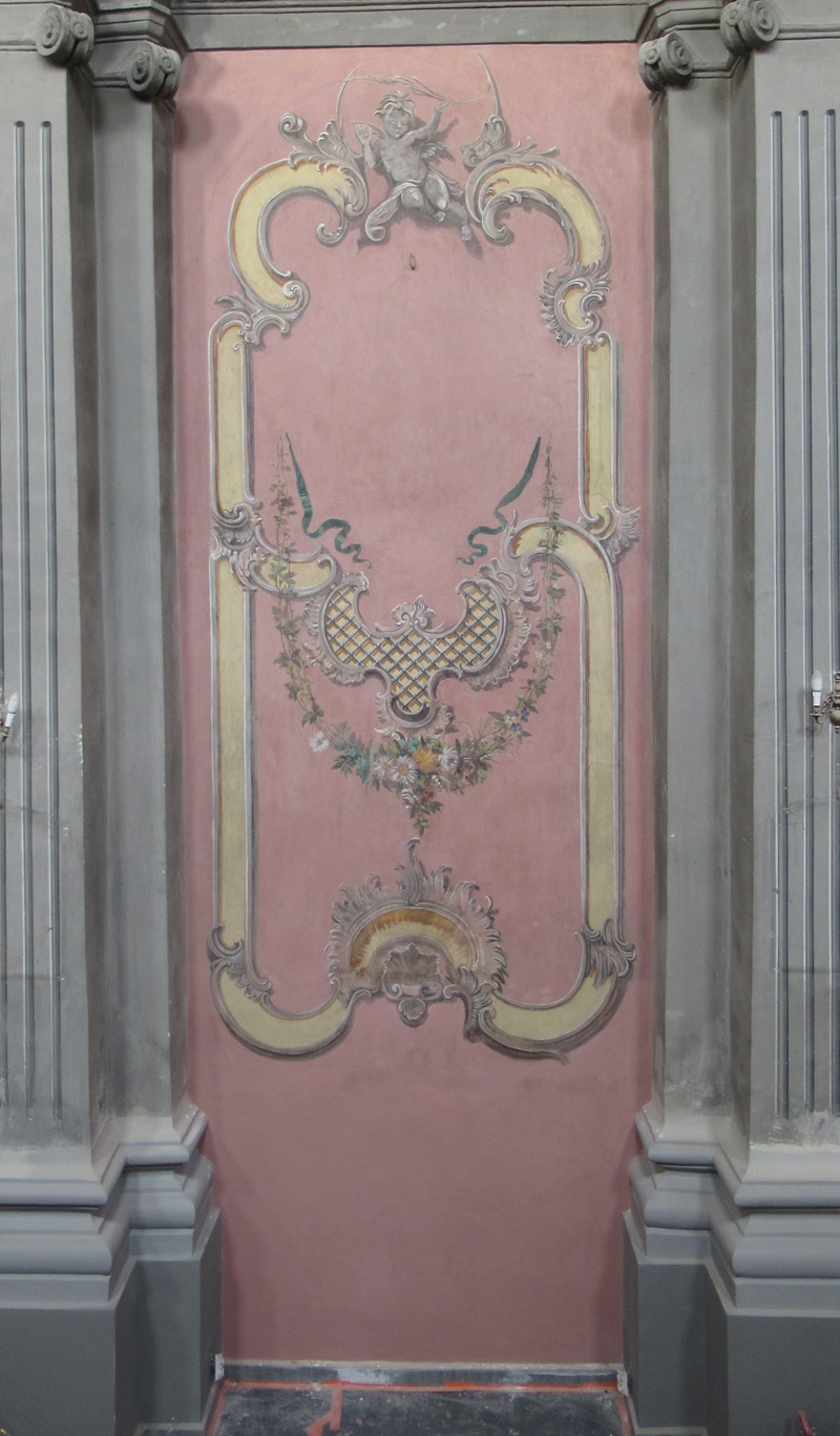 Fragment ściany kościoła z odrestaurowaną polichromią ścienną z XIX wieku, przedstawiającą dekoracyjne ornamenty roślinne, aniołka i geometryczne wzory w odcieniach beżu, różu i zieleni, otoczone...