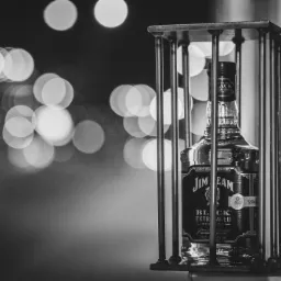 Czarno-białe zdjęcie butelki Jim Beam Black Extra Aged w metalowej klatce, z rozmytym tłem świateł.
