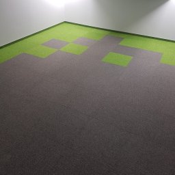 ALTON PIOTR ŁUCZAK - Szara wykładzina dywanowa w biurze z wstawkami z zielonych kwadratów przy ścianach, oświetlona światłem naturalnym wpadającym z góry.