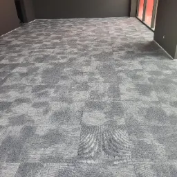 Ułożona szara wykładzina dywanowa w kwadratach w pustym pomieszczeniu z ciemnymi ścianami i oknem z czerwonymi ramami.