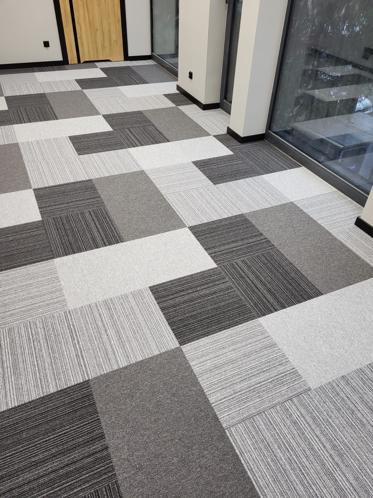 Wzór podłogi z kwadratowych płytek w odcieniach szarości, ułożonych naprzemiennie, w nowoczesnym biurze z dużymi oknami.