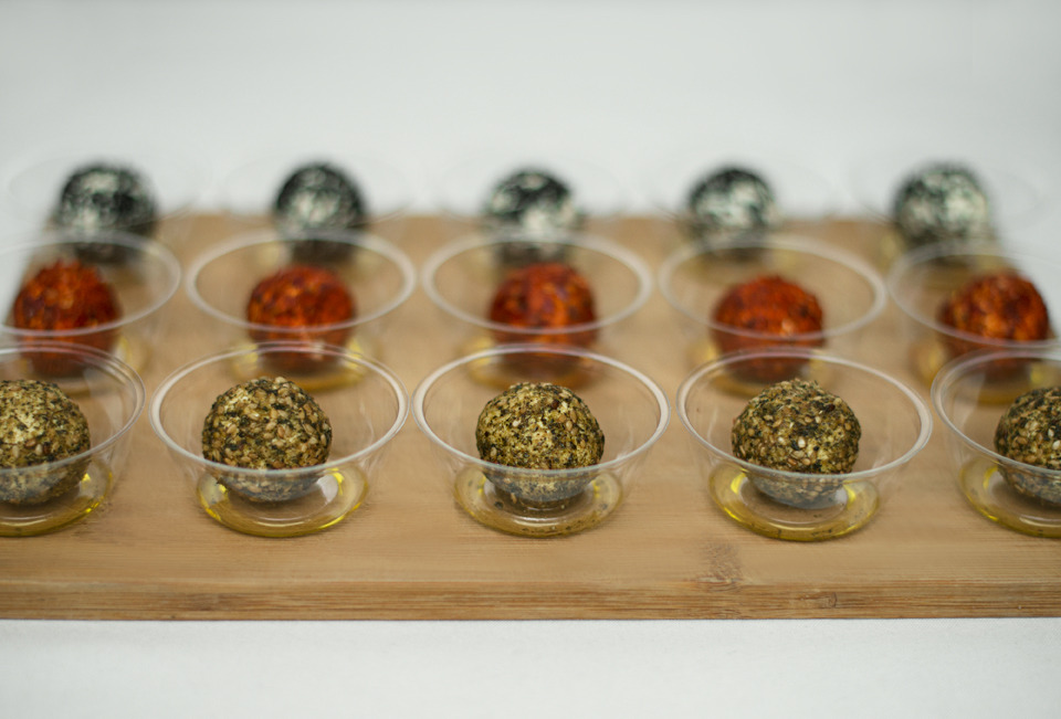 Dekoracyjne kulki serowe w trzech smakach (czarny pieprz, papryka, zioła) podane w przezroczystych kieliszkach na drewnianej desce.