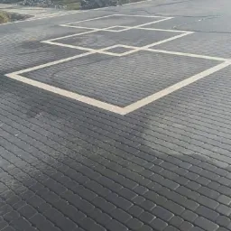 Świeżo ułożona, ciemnoszara kostka brukowa z jasnymi, kwadratowymi obramowaniami, tworzącymi geometryczny wzór na podjeździe.