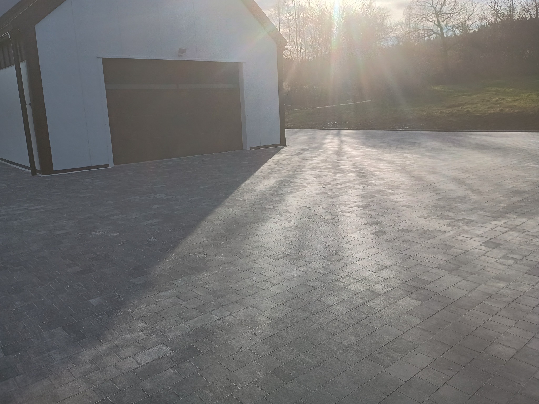Nowa, szara kostka brukowa ułożona przed budynkiem z garażem, widok w słoneczny dzień.