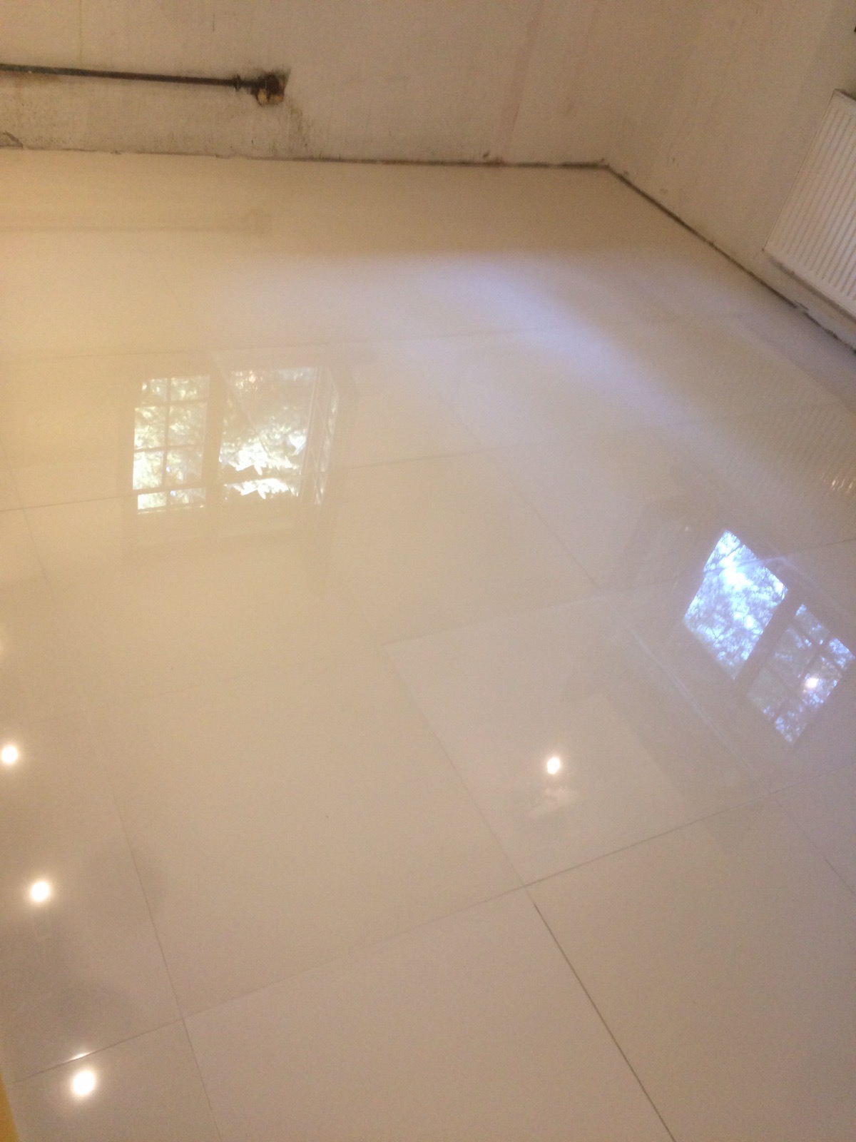 Błyszcząca, kremowa podłoga z płytek w pustym pomieszczeniu, odbijająca światło i widok z okna.