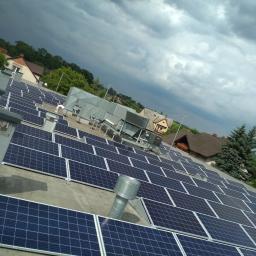 LMV Group - Rozległa instalacja paneli słonecznych na płaskim dachu budynku, widok z góry, pochmurne niebo w tle.