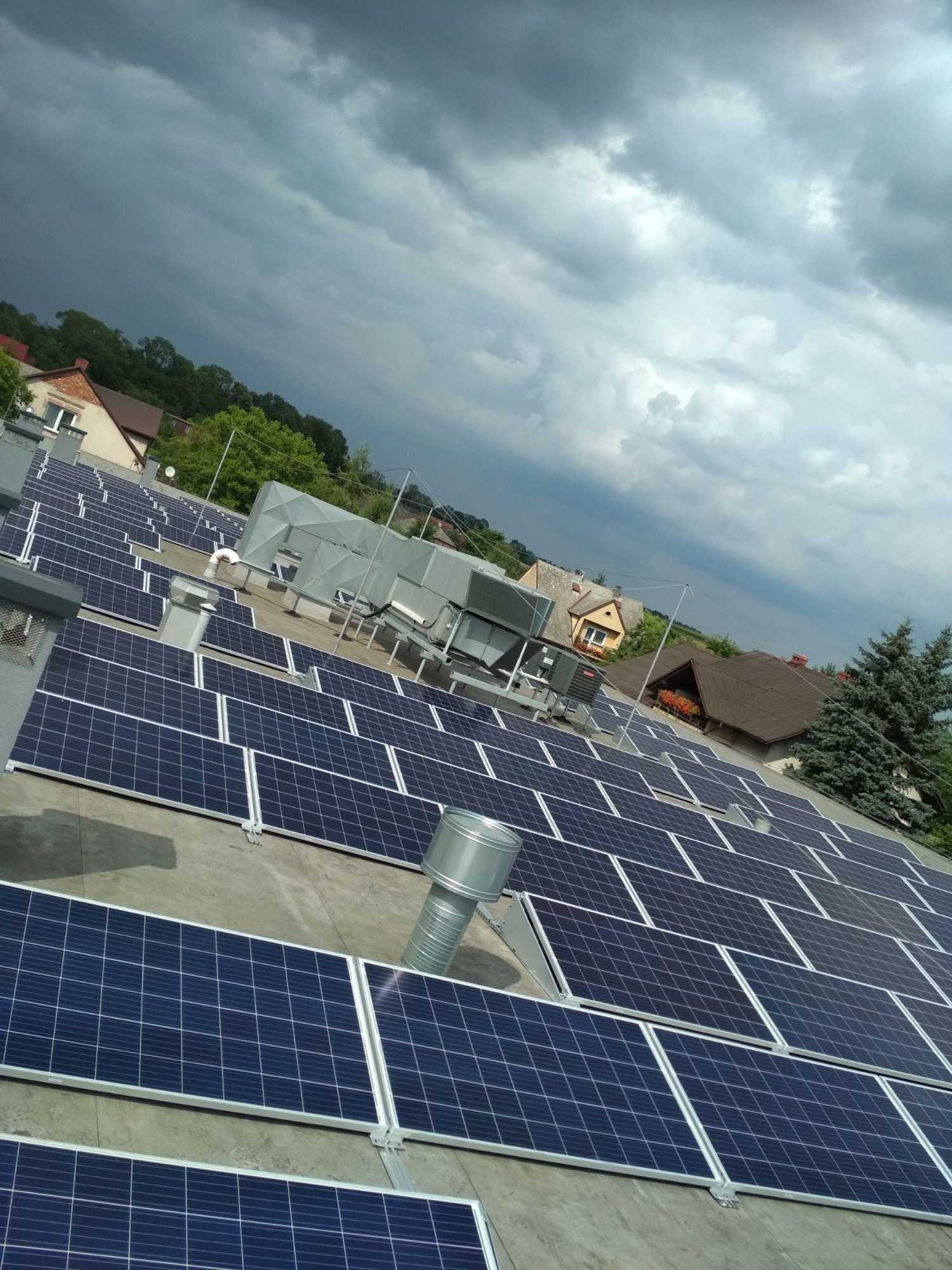 Rozległa instalacja paneli słonecznych na płaskim dachu budynku, widok z góry, pochmurne niebo w tle.