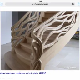 Drewniane schody z rzeźbioną balustradą o motywie gałęzi drzew, widok z dołu na górę, jasne drewno, naturalne światło.