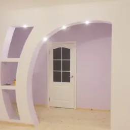 Wykończone wnętrze z łukowym przejściem i półkami z płyty gipsowo-kartonowej, oświetleniem punktowym i delikatnym fioletowym malowaniem ścian, widoczna biała stolarka drzwiowa.