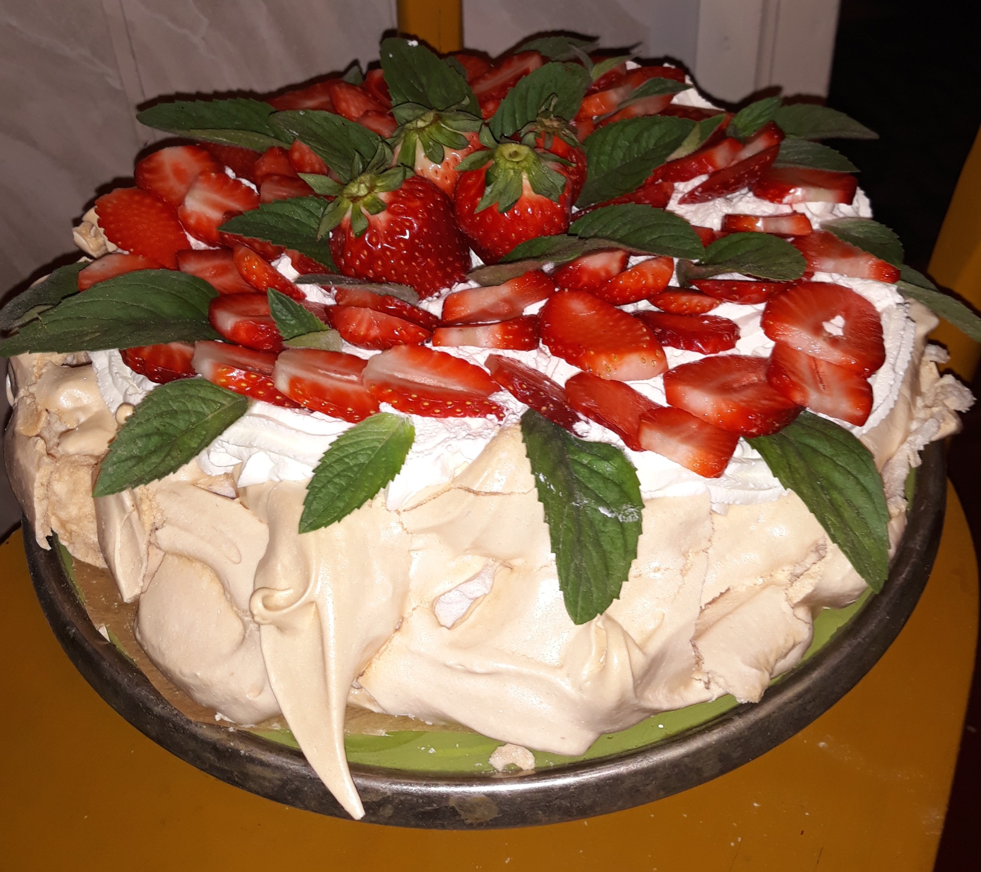 Tort bezowy Pavlova udekorowany świeżymi truskawkami i listkami mięty na metalowej tacy.