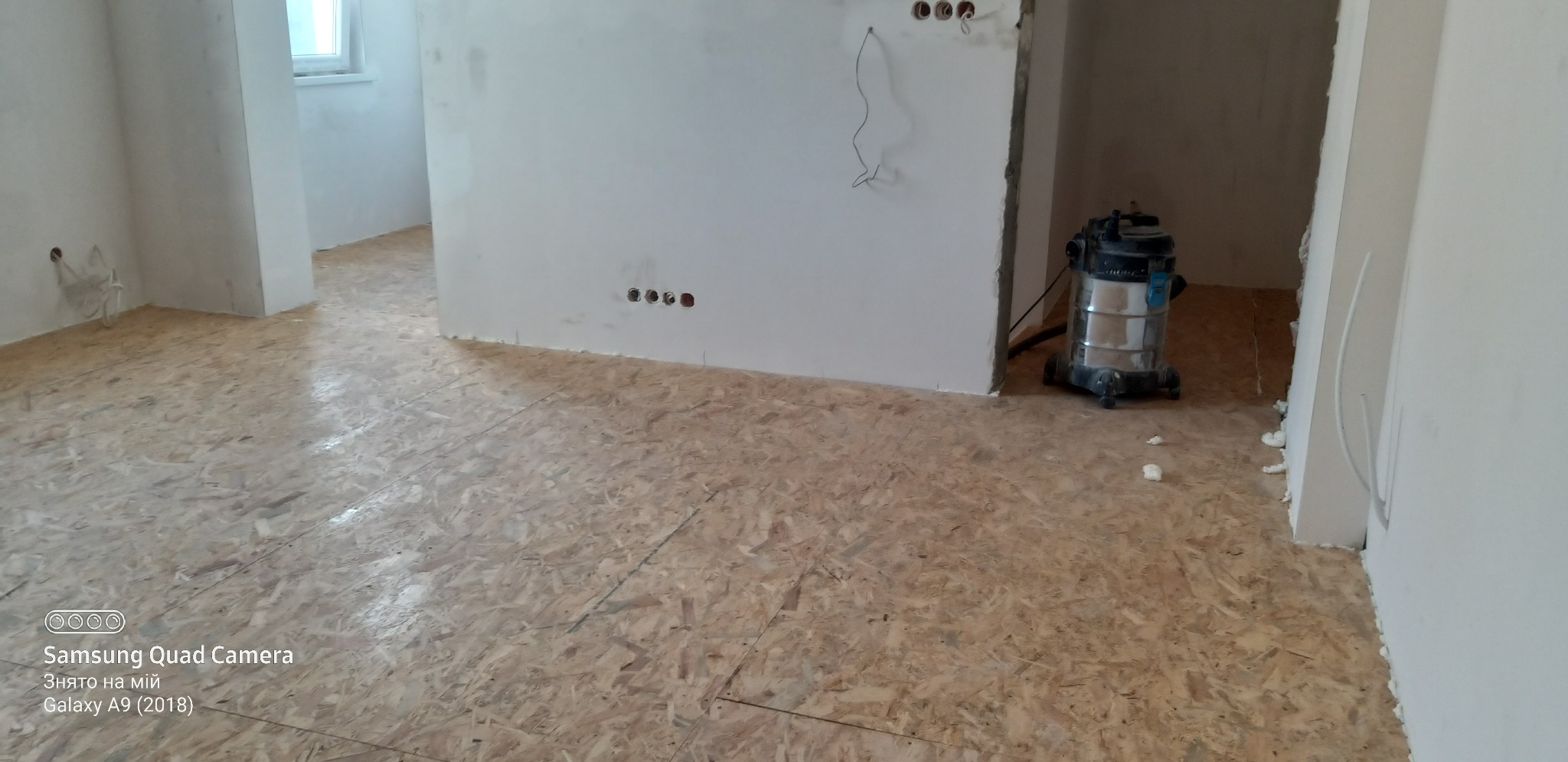 Przygotowanie podłogi z płyt OSB w trakcie remontu mieszkania, widoczny odkurzacz przemysłowy i niedokończone ściany.