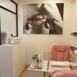 Wnętrze salonu kosmetycznego z białymi meblami, różowym krzesłem i dużym plakatem ust na ścianie.