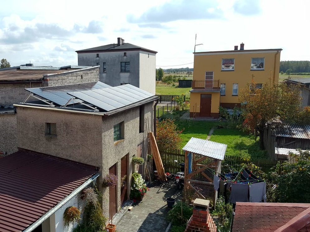 Panele słoneczne na dachu dwukondygnacyjnego budynku gospodarczego w wiejskiej scenerii, widok z góry.