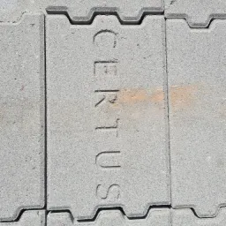 Szara, betonowa nawierzchnia ułożona z pojedynczych elementów z wyżłobionym napisem 'CERTUS', widoczne delikatne zabrudzenia.