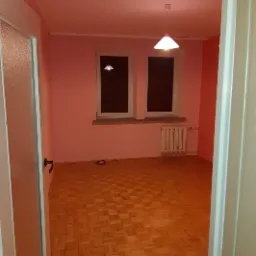 Pokój z parkietem w jodełkę, świeżo pomalowany na różowo, widok zza otwartych drzwi, grzejnik pod oknem.