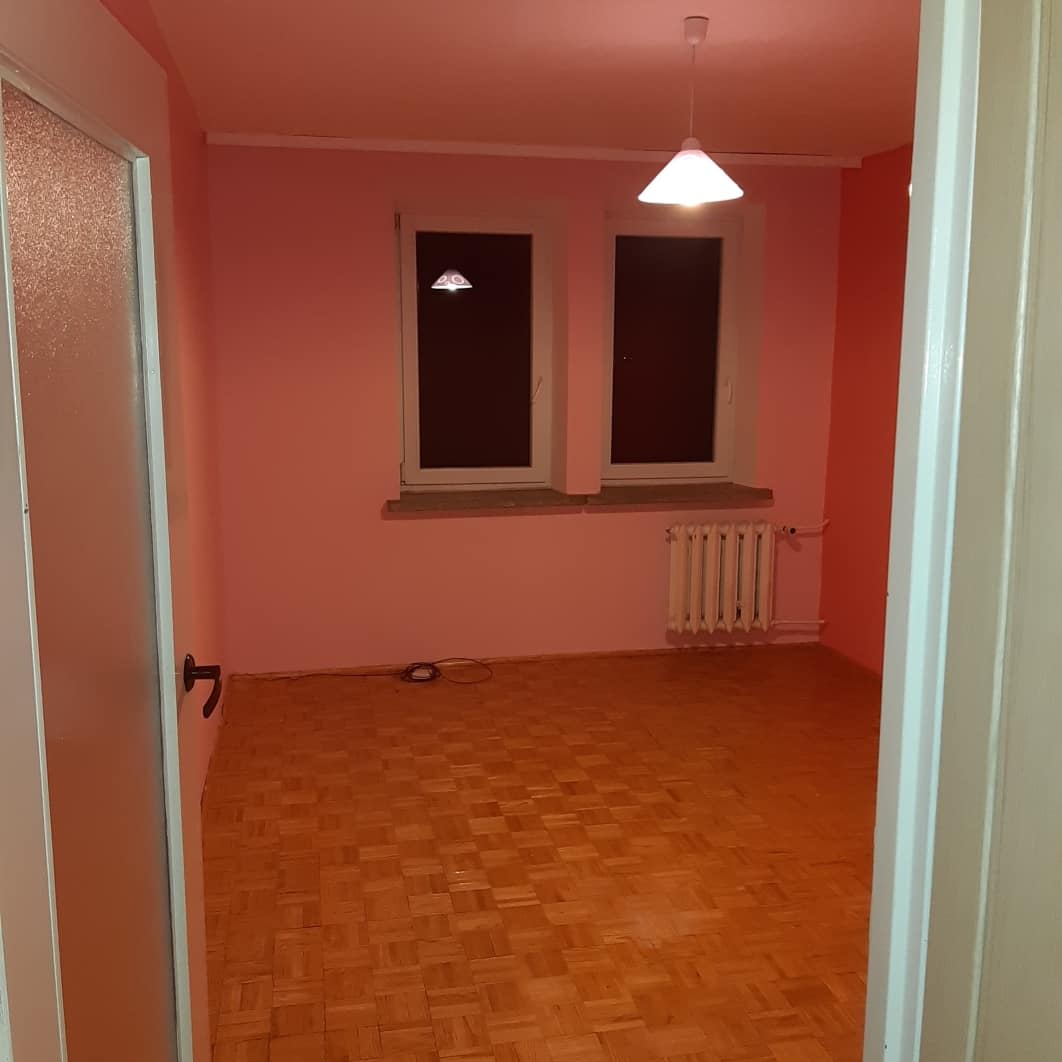 Pokój z parkietem w jodełkę, świeżo pomalowany na różowo, widok zza otwartych drzwi, grzejnik pod oknem.