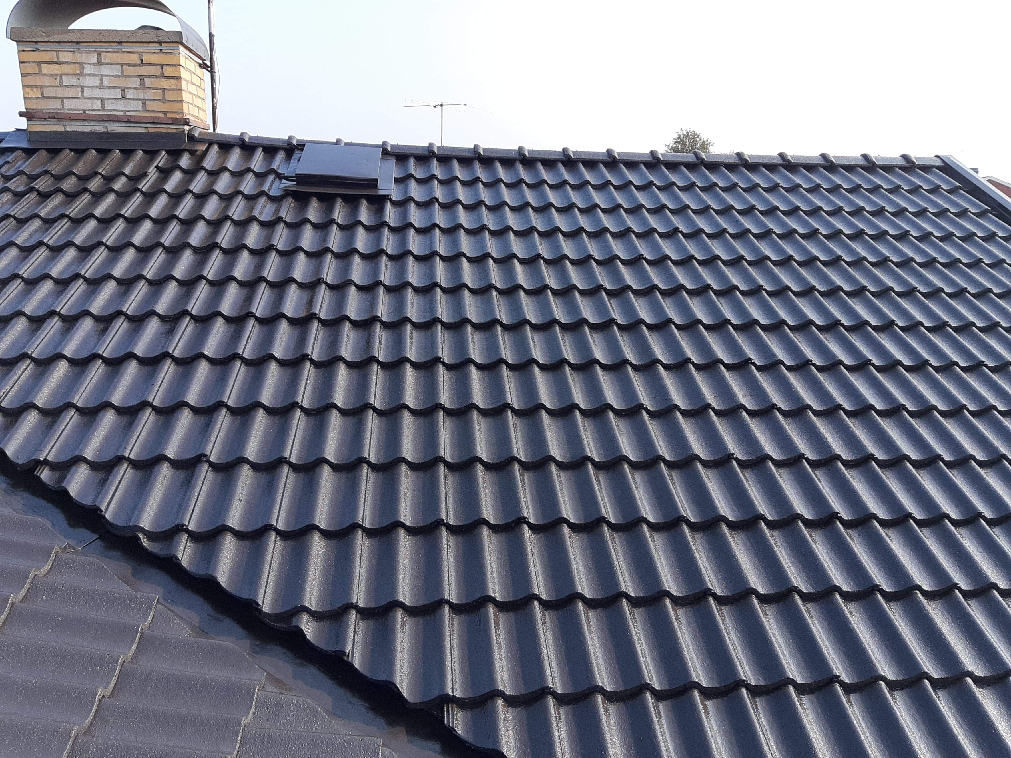 Błyszczący, czarny dach z dachówki ceramicznej, widoczny komin z cegły i antena telewizyjna.