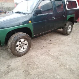 Ciemnozielony pickup z białą zabudową na pace, zaparkowany na ubitej ziemi, widoczne błotniste opony i ślady korozji na progach.