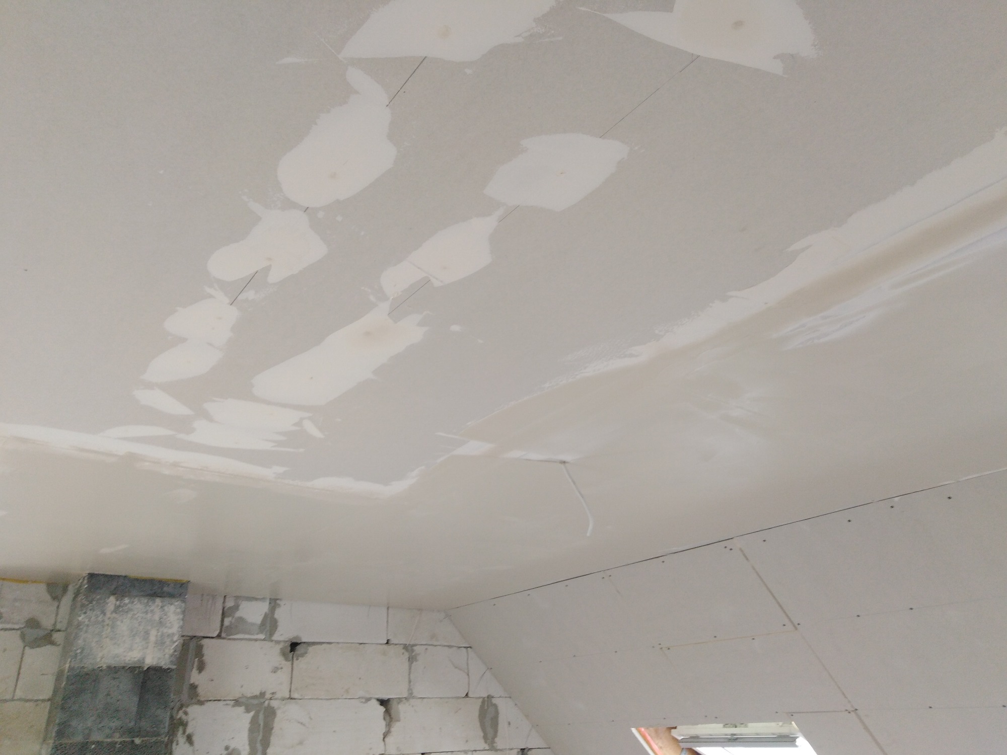 Poddasze w trakcie prac wykończeniowych: sufit z płyt gipsowo-kartonowych ze śladami po szpachlowaniu, widoczne łączenia i niedoskonałości, fragment ściany z białego bloczka.