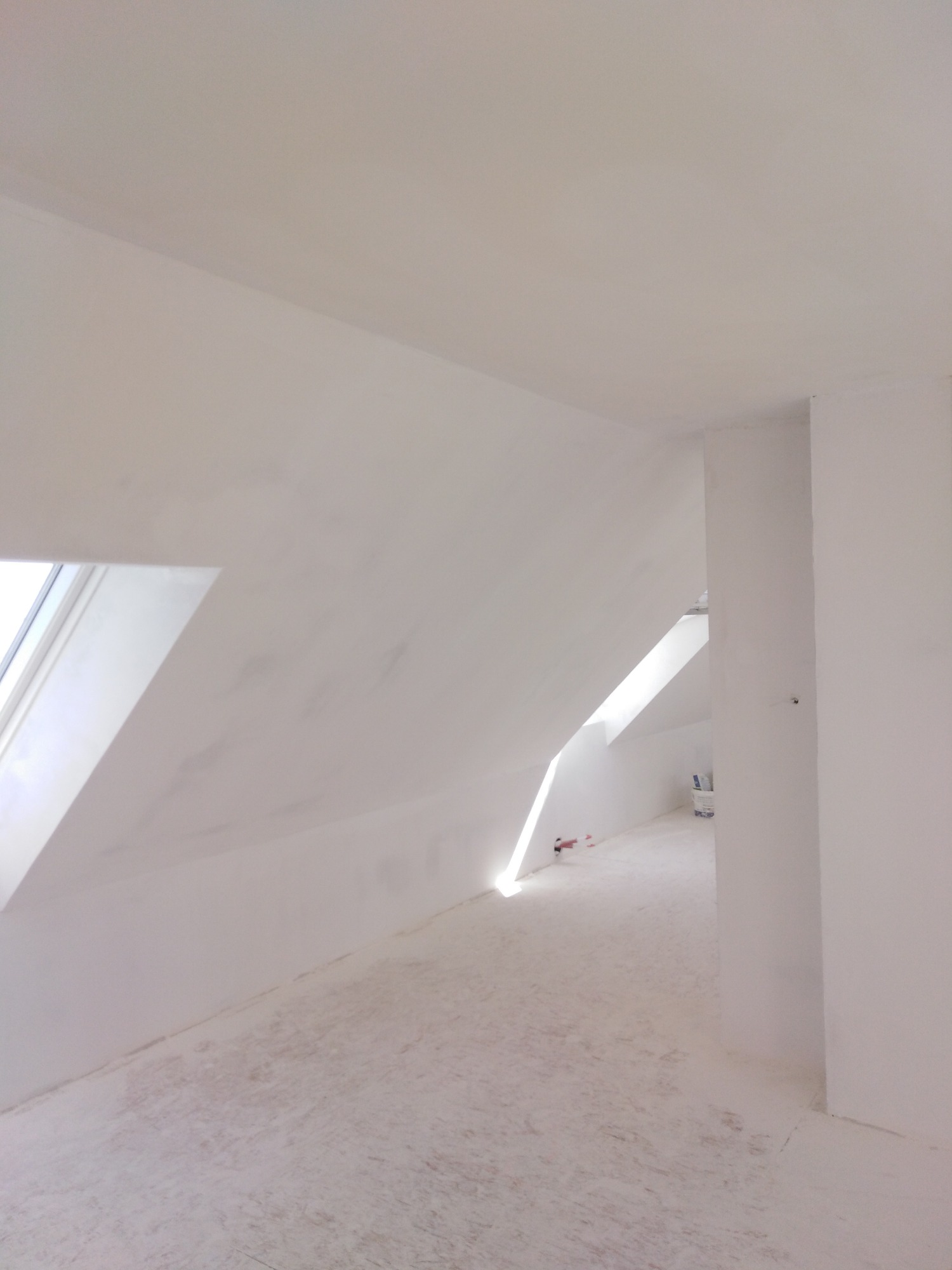 Poddasze po nałożeniu gładzi, widoczne okno dachowe i nierówności na podłodze zabezpieczonej folią.