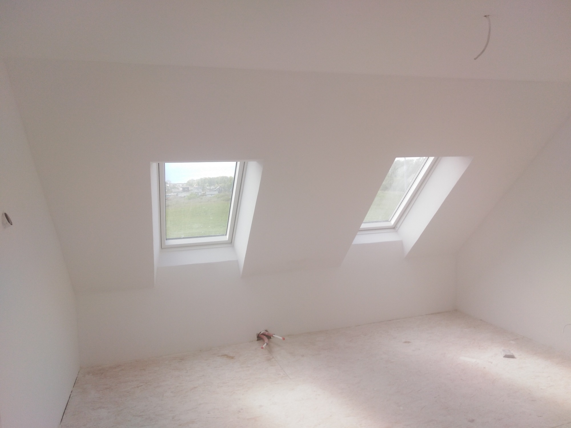 Poddasze po malowaniu na biało z dwoma oknami dachowymi, widoczne ślady po pracach na podłodze i wystające przewody elektryczne.