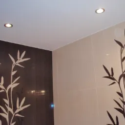 Wykończona ściana łazienki z jasnymi i ciemnymi płytkami z motywem bambusa, oświetlona dwoma punktowymi lampami sufitowymi.