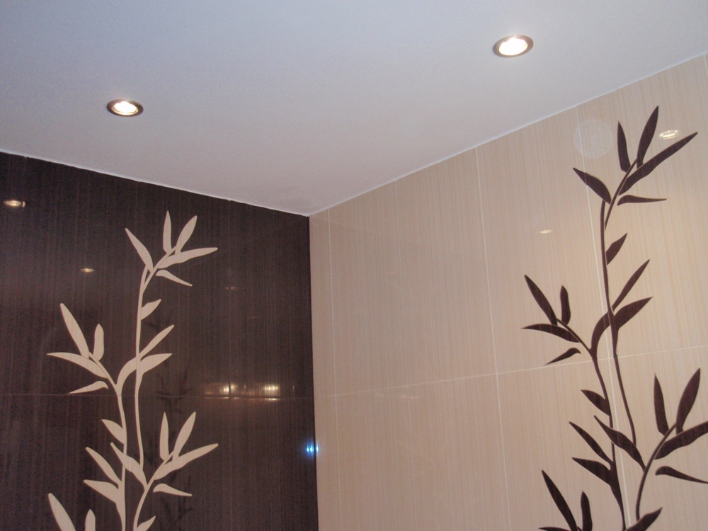 Wykończona ściana łazienki z jasnymi i ciemnymi płytkami z motywem bambusa, oświetlona dwoma punktowymi lampami sufitowymi.