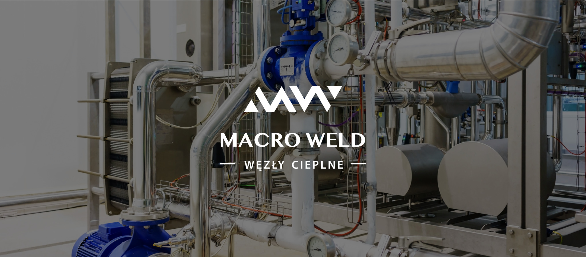 Kompleksowa instalacja węzła cieplnego z widocznym wymiennikiem ciepła płytowym, rurami ze stali nierdzewnej, zaworami i manometrami, z nałożonym logo firmy Macro Weld.