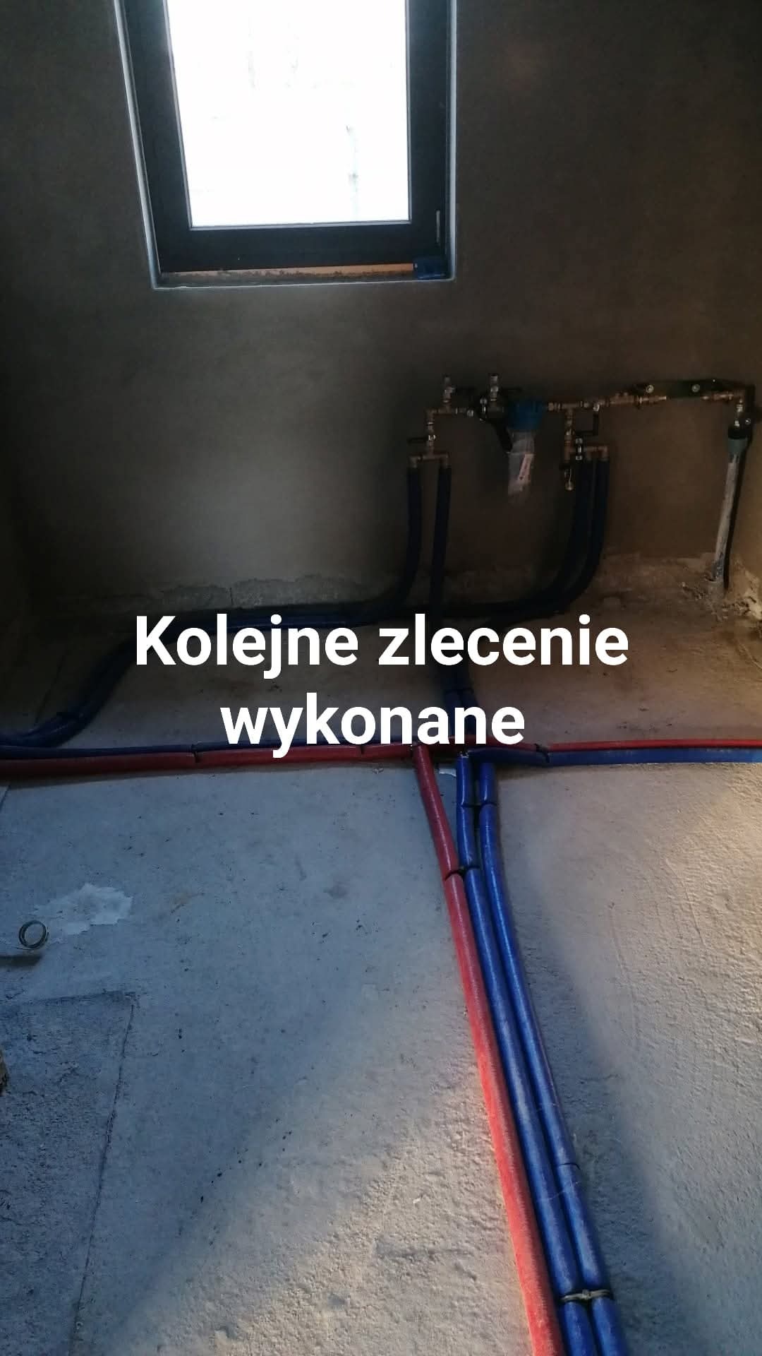 Instalacja wodna i grzewcza w surowym wnętrzu, Grońsko. Widoczne rury w kolorach niebieskim i czerwonym, oraz okno w górnej części kadru.
