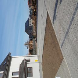 DAR-KOP - Ułożona szara kostka brukowa na nowym osiedlu, z przygotowanym pasem ziemi obok, w tle budowa domów i maszyny budowlane.