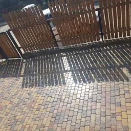 DAR-KOP - Wibrująca zagęszczarka obok nowo ułożonej, wielokolorowej kostki brukowej w odcieniach beżu, brązu i szarości, z cieniem drewnianego płotu rzucanym na powierzchnię.