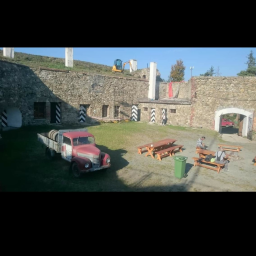 DAR-KOP - Dziedziniec starego kamiennego budynku z odrestaurowanymi elementami, gdzie stoi czerwona ciężarówka z beczkami na pace, a na górze widać małą koparkę.