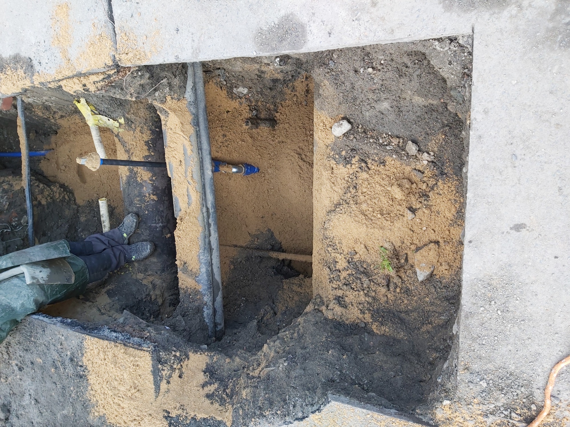 Odkrywka ziemna w Bielawie z widocznymi rurami instalacji wodno-kanalizacyjnej i fragmentem roboczych butów oraz łopaty.