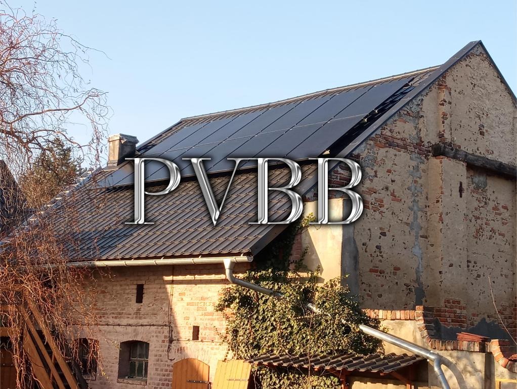 Panele słoneczne na dachu starego, ceglanego domu z widocznymi uszkodzeniami elewacji i roślinnością pnącą się po ścianie.