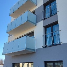 F.H.U.TIG Krzysztof Misiak - Nowoczesny budynek z balkonami z balustradami szklanymi i metalowymi. Ujęcie z dołu, błękitne niebo w tle. Widoczne detale wykończenia elewacji.