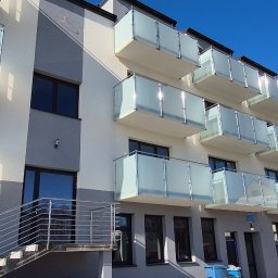 F.H.U.TIG Krzysztof Misiak - Nowoczesny budynek z balkonami z mlecznego szkła i metalowymi poręczami schodów zewnętrznych. Jasne, słoneczne ujęcie.