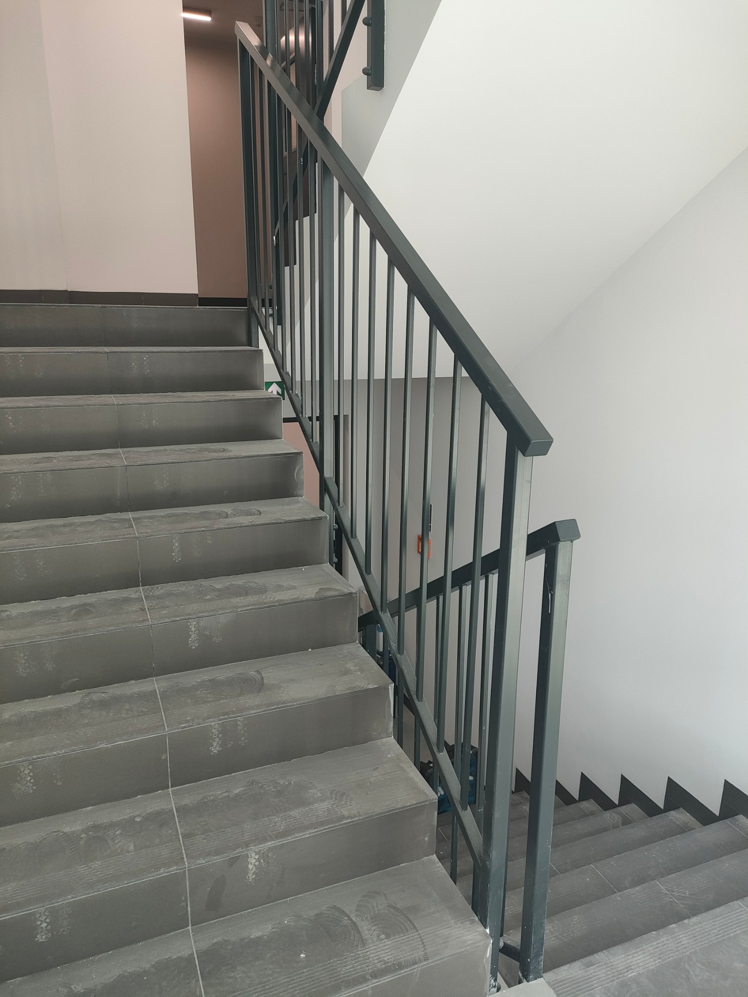 Metalowa poręcz schodowa w budynku w trakcie budowy, widoczne ślady budowlane na schodach.