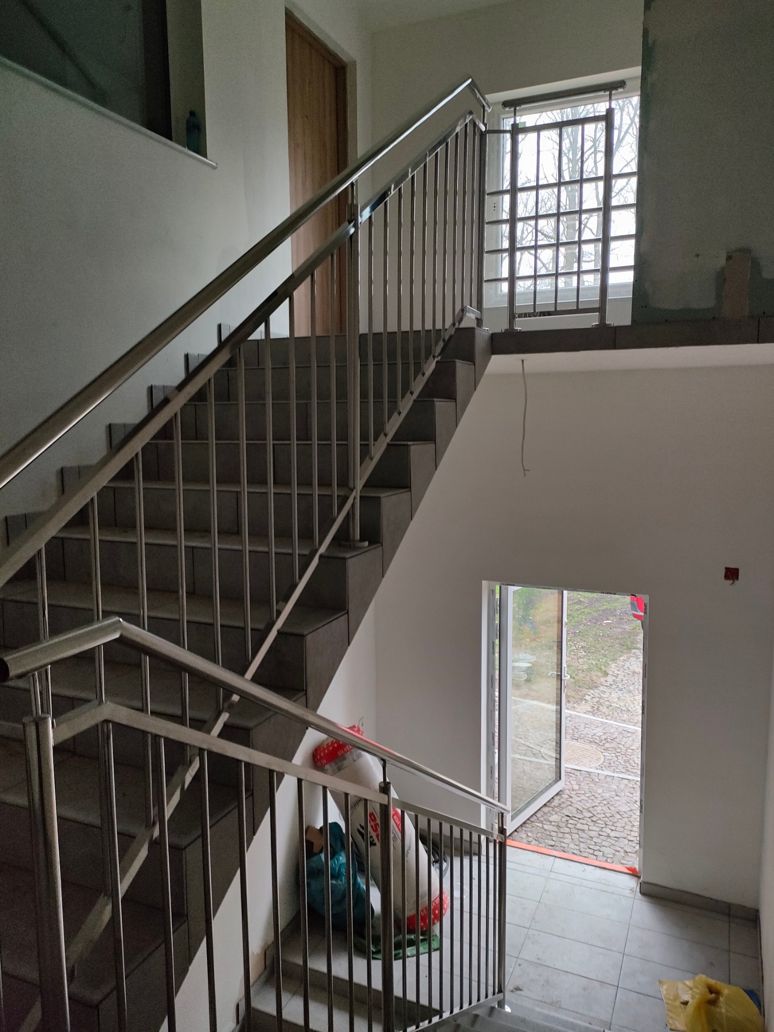 Schody wewnętrzne z zamontowaną metalową poręczą w budynku w Sadkowie, widoczne ślady prac wykończeniowych.