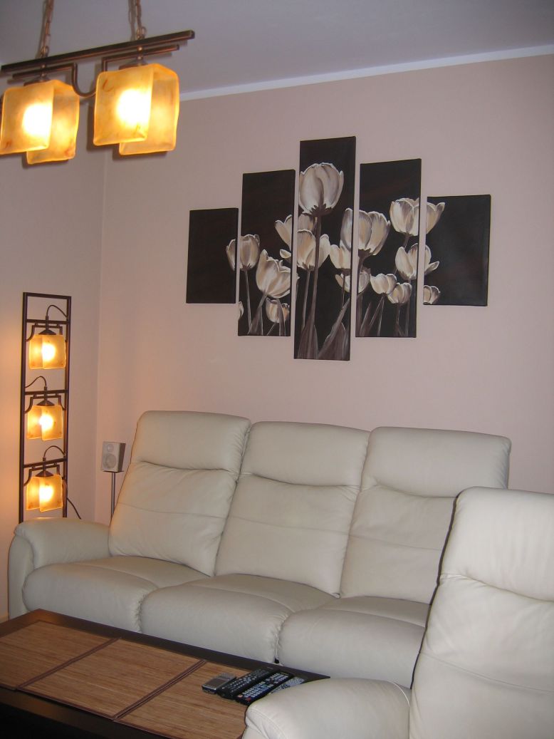 Fotoobraz z motywem białych tulipanów, składający się z pięciu paneli, zawieszony nad jasną, skórzaną sofą w salonie, oświetlony lampą stojącą i wiszącą.