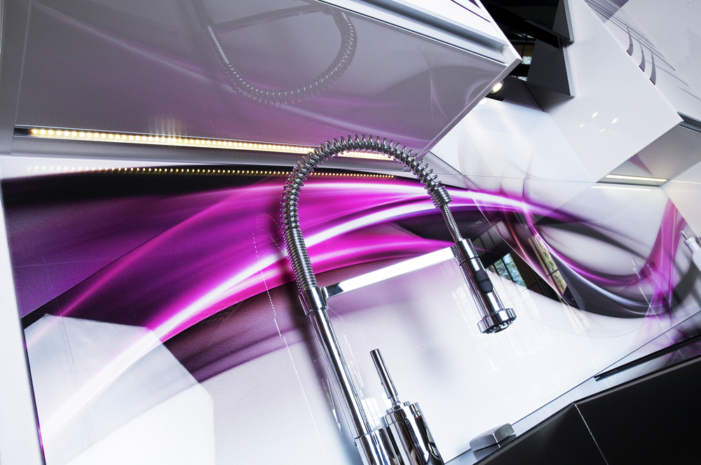 Nowoczesna kuchnia z panelami szklanymi z grafiką w odcieniach fioletu i białym blatem, chromowana bateria z elastyczną wylewką i oświetlenie LED pod szafkami.