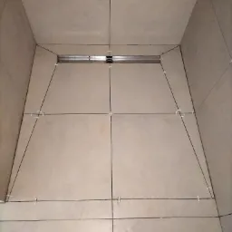 Podłoga prysznicowa w trakcie układania płytek z widocznym odpływem liniowym i krzyżykami dystansowymi w spoinach.