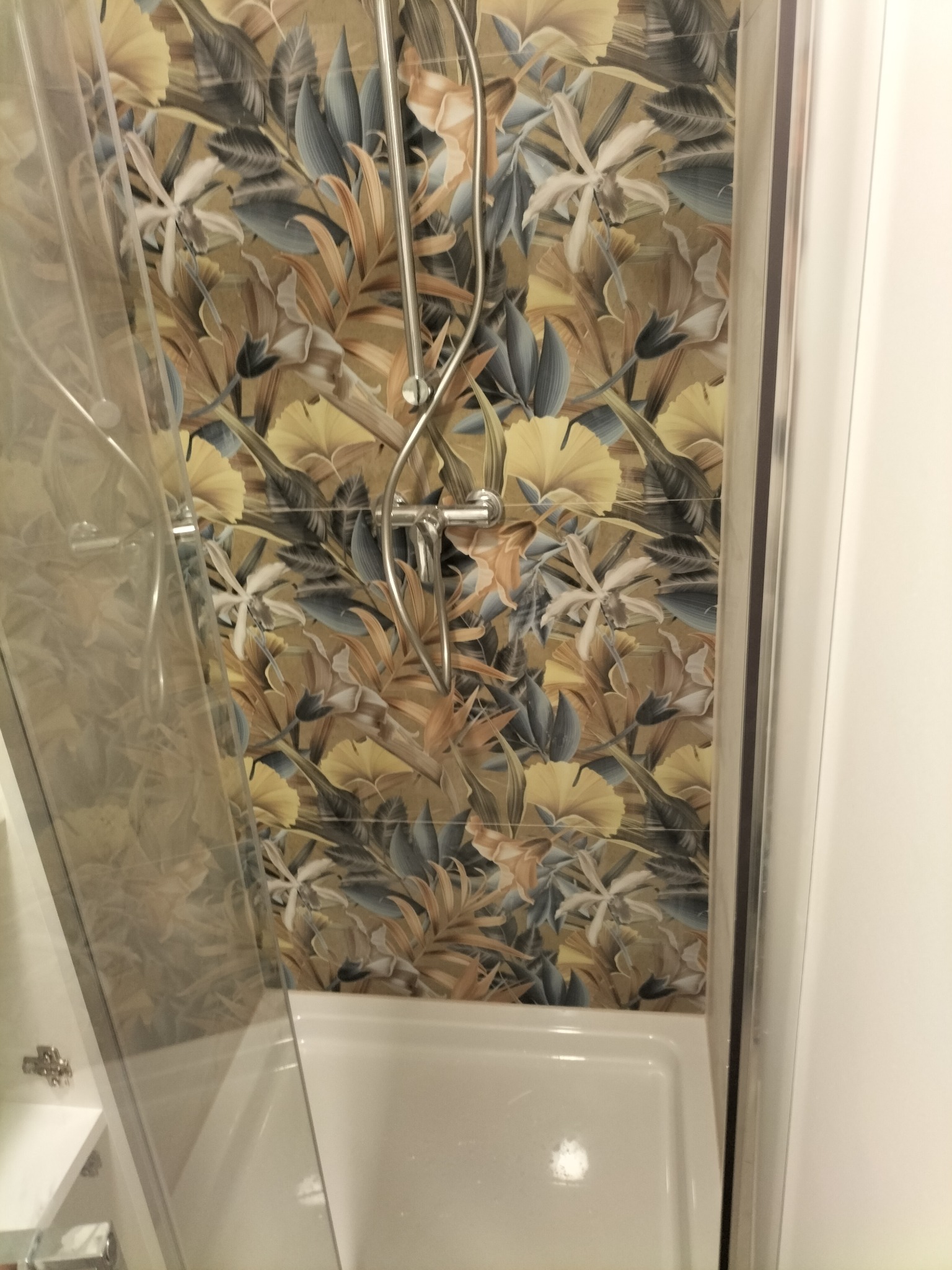 Kabina prysznicowa z deszczownicą i baterią, na ścianie wzorzyste płytki w motywy kwiatowe i liściaste w odcieniach beżu, brązu, szarości i bieli.