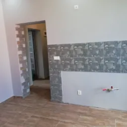 Płytki ceramiczne na ścianie i podłodze w trakcie remontu, widoczne instalacje wodne i elektryczne, surowy stan wykończenia.