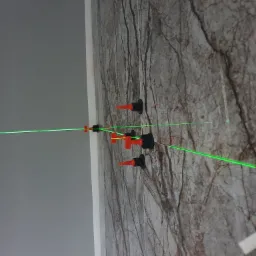 Układanie płytek imitujących marmur na ścianie, widoczny laserowy poziom i system poziomowania płytek z czerwonymi klinami i czarnymi podstawkami.